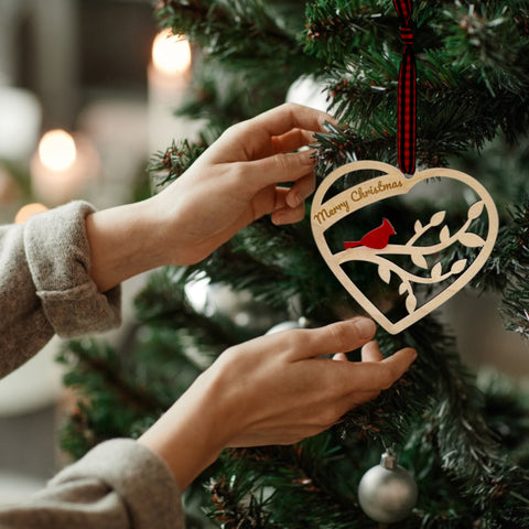 A wooden heart-shaped ornament adorned with intricate carvings. The words 'Merry Christmas' are elegantly engraved across the top of the heart. This memorial ornament captures the spirit of Christmas with its heartfelt design.